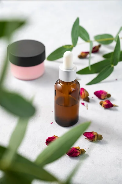 stock image Face or body cream and serum in bottle with rose and eucalyptus on a light background close up. The concept of care cosmetics with herb. Health and beauty. 