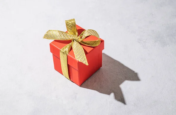 A red gift box with a gold ribbon on a gray background with shadow. The concept of holiday photography. Surprise for Valentine\'s Day, birthday, wedding. Copy space and top view.