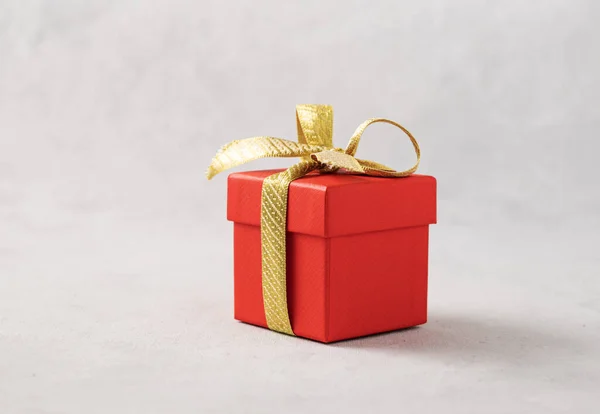 A red gift box with a gold ribbon on a gray background. The concept of holiday photography. Surprise for Valentine\'s Day, birthday, wedding. Copy space and front view.