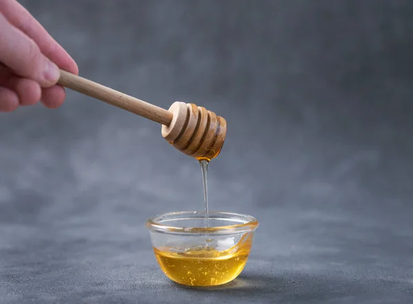 Honey flows from a wooden stick into a glass bowl on a dark background close-up. The concept of healthy and organic food. Front view and free space for text.