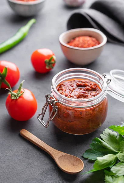 stock image Homemade tomato sauce for pizza or pasta in a jar on a dark background with fresh vegetables, herbs and spicy close up. The concept of classic Italian cuisine