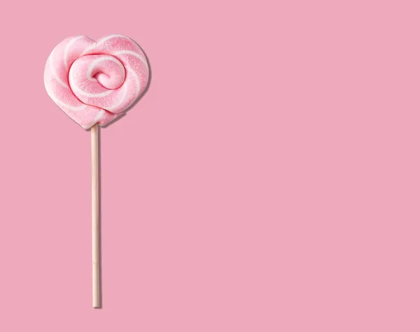 Pink lollipop in the form of a heart on a stick on a pastel pink background. Free space for text.