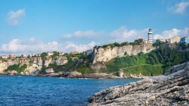 Güneşli bir yaz gününde deniz manzarası ve renkli evler ve ağaçlarla dolu bir uçurumda deniz feneri. Sile, Türkiye