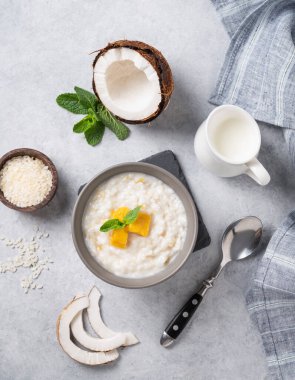 Hindistan cevizi sütlü pirinç lapası ve mavi arka planda mango dilimleri. Besleyici ve tatmin edici gıda kavramı. Güneydoğu Asya ülkelerinde kahvaltı veya tatlı için popüler bir yemek.