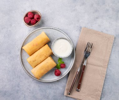 Peçeteli, arka planda hafif bir tabakta ahududu ve ekşi kremalı ev yapımı krep. Sağlıklı gıda konsepti. Üst görünüm ve kopyalama alanı.