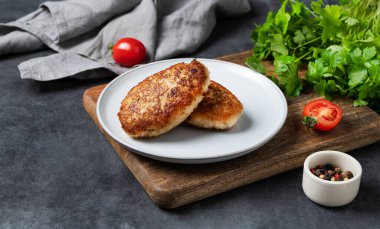 Koyu bir zeminde, üzerinde taze domates ve bitkiler olan kızarmış et pirzolası. Ev yapımı sağlıklı ve lezzetli yemekler. Metin için boş alan.