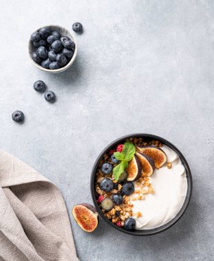 Doğal yoğurt, müsli, böğürtlen ve incir. Mavi arka planda, peçeteli. Sağlıklı ve besleyici bir kahvaltı. Üst görünüm ve özet kopyala.