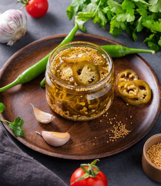 Jalapeno acı biberi, bir kavanozda dilimlenmiş, ahşap tabakta baharatlar ve koyu arkaplanda taze sebzeler. Sebzeli vejetaryen atıştırması. Geleneksel Meksika mutfağı. 