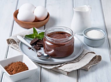 Hafif ahşap arka planda, içinde malzemeler olan bir kavanozda nefis çikolatalı puding. Ev yapımı sağlıklı çikolatalı mus konsepti.