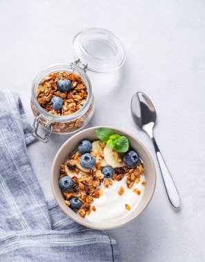 Vejetaryen yoğurtlu müsli, muz ve yaban mersinli hafif bir arka planda. Kahvaltı için sağlıklı ve besleyici ev yapımı tahıl gevreği. Metin için üst görünüm ve boş alan.
