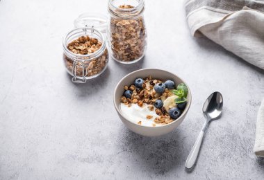 Gri arka planda bir kasede muzlu ve yaban mersinli vejetaryen yoğurdu olan müsli. Kahvaltı için sağlıklı ve besleyici ev yapımı tahıl gevreği. Metin için boş alan.