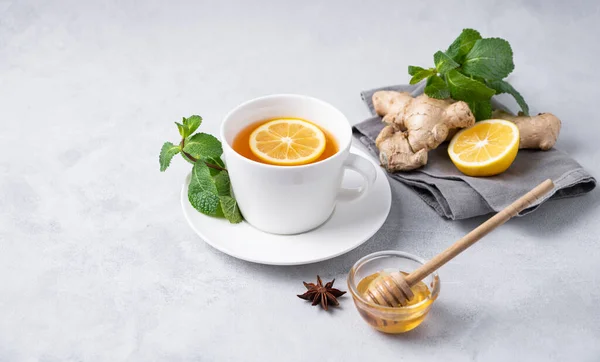 stock image A cup of tea with fresh lemon, honey, mint and ginger on a light background. The concept of a healthy drink for immunity. Free space for text.