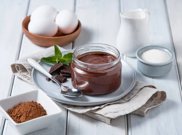 Delicious chocolate pudding in a jar on a light wooden background with ingredients. The concept of homemade healthy chocolate mousse.