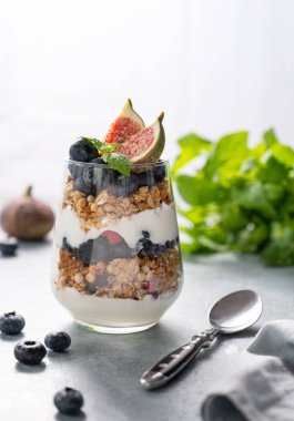 Lezzetli doğal yoğurtlu granola ve mavi arka planda bir bardak böğürtlen. Sağlıklı ve besleyici bir kahvaltı. Diyet yemek. Ön görünüm ve boşluk kopyala