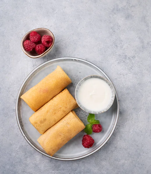 Homemade crepes with raspberry and sour cream on a plate on a light background. Healthy food concept. Top view and copy space.