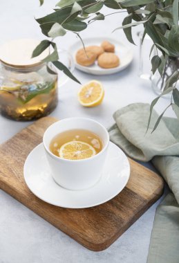 Limonlu bitki çayı ve okaliptüs dalları ve çaydanlıkla birlikte hafif bir zemin üzerinde beyaz bir fincanda nane çayı. Dokunulmazlık için sağlıklı ve lezzetli içecek konsepti.