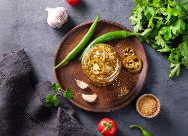 Jalapeno acı biberi, bir kavanozda dilimlenmiş, ahşap tabakta baharatlar ve koyu arkaplanda taze sebzeler. Sebzeli vejetaryen atıştırması. Geleneksel Meksika mutfağı. Üst görünüm.