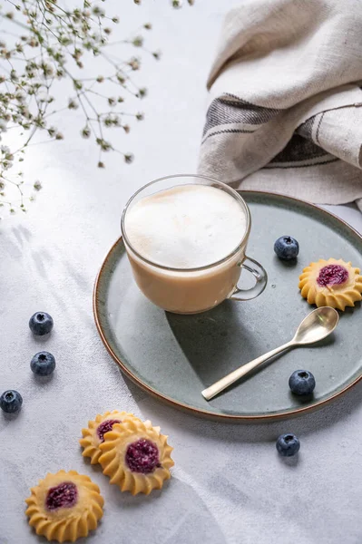 Cappuccino ya da sütlü sütlü latte kahve ev yapımı çilekli kurabiye ve yaban mersinli hafif bir arka planda çigila dallarıyla. Bahar sabahı kahvaltısı kavramı. Üst görünüm.