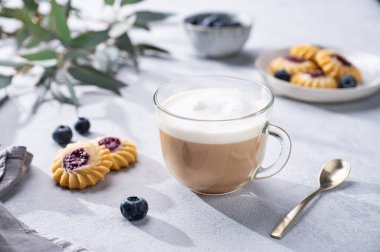 Kapuçino ya da süt köpüklü latte ev yapımı çilekli kurabiye ve okaliptüs dallı hafif bir arka planda yabanmersini. Bahar sabahı kahvaltısı hariç.. 
