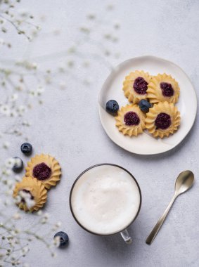 Kapuçino ya da sütlü sütlü latte kahve. El yapımı çilekli kurabiye ve yaban mersinli ve çigila dallı. Bahar sabahı kahvaltısı kavramı. Üst görünüm
