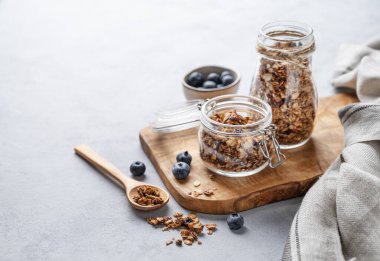 Fındıklı ev yapımı tahıl gevreği ve hafif arka planda bir kavanozda taze yaban mersini. Kahvaltıda sağlıklı vejetaryen müsli. Metin için boş alan.