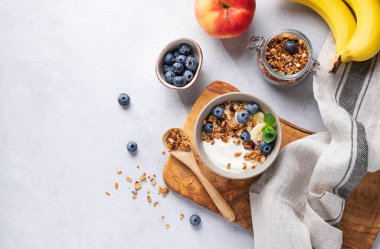 Yoğurt ve yaban mersinli ev yapımı granola. Arka planda taze böğürtlen, muz ve elma var. Müsli ile sağlıklı vejetaryen kahvaltısı. Üst görünüm ve kopyalama alanı.