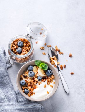 Vejetaryen yoğurtlu müsli, muz ve yaban mersinli hafif bir arka planda. Kahvaltı için sağlıklı ve besleyici ev yapımı tahıl gevreği. Metin için üst görünüm ve boş alan.
