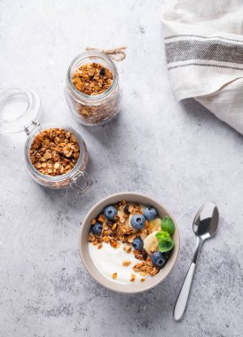 Vejetaryen yoğurtlu müsli, muz ve yaban mersinli gri dokuya sahip bir kasede. Kahvaltı için sağlıklı ve besleyici ev yapımı tahıl gevreği. Metin için üst görünüm ve boş alan.