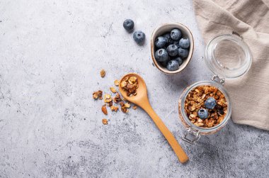 Fındıklı ev yapımı tahıl gevreği ve hafif arka planda bir kavanozda taze yaban mersini. Kahvaltıda sağlıklı vejetaryen müsli. Metin için üst görünüm ve boş alan.