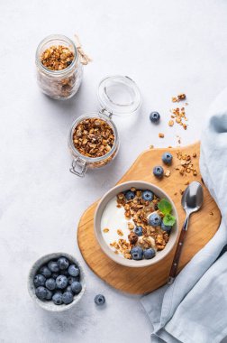 Yoğurt, granola ve hafif arkaplanda taze yaban mersinli sağlıklı bir kahvaltı konsepti. Ev yapımı diyet ve protein yiyeceği. Üst görünüm ve kopyalama alanı.