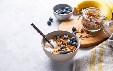 Yoğurt, tahıl gevreği, taze yaban mersini ve muzdan oluşan sağlıklı bir kahvaltı konsepti. Ev yapımı diyet ve protein yiyeceği. Metin için boş alan.
