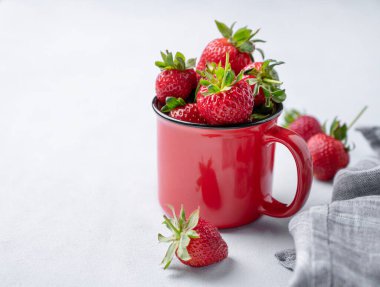 Kırmızı bardaktaki sulu çilekler hafif arka planda ve peçeteli. Çiftlik olgun, sağlıklı meyveler. Metin için boş alan.