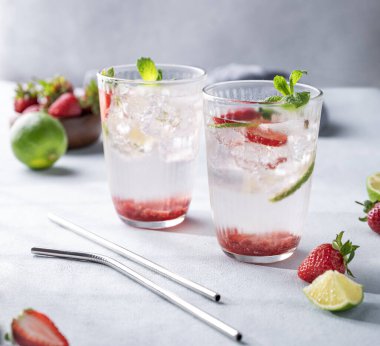 Böğürtlen, kireç, nane ve buzlu bardakta taze çilekli mojito ve metalik tüp. Bir parti için yaz tazeleyici içecek konsepti. Ön görünüm.