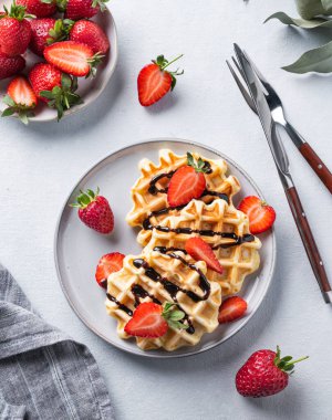 Taze çilekli ev yapımı waffle ve hafif arkaplanlı bir tabakta çikolata. Geleneksel Belçika waffle 'ları. Sağlıklı kahvaltı. Üst görünüm.