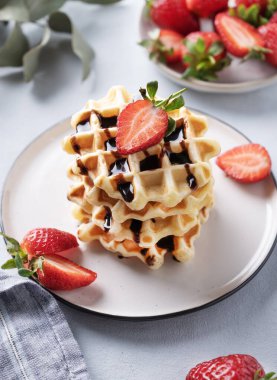 Taze çilekli ev yapımı waffle 'lar ve arka planda hafif bir tabakta bir yığın çikolata. Geleneksel Belçika waffle 'ları. Sağlıklı kahvaltı. Üst görünüm.