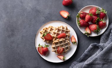 Koyu arkaplanda taze çilekli ev yapımı waffle 'lar. Geleneksel Belçika waffle 'ları. Sağlıklı vejetaryen kahvaltısı. Üst görünüm ve kopyalama alanı.