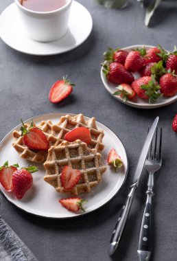 Taze çilek ve pudra şekerli ev yapımı waffle 'lar koyu bir arka planda bir fincan çayla birlikte. Geleneksel Belçika waffle 'ları. Sağlıklı kahvaltı.. 