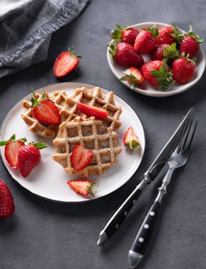 Koyu arkaplanda taze çilek ve pudra şekerli ev yapımı waffle 'lar. Geleneksel Belçika waffle 'ları. Sağlıklı vejetaryen kahvaltısı. 