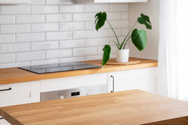 Ürün montajı için boş alanı olan ahşap masa üstü ya da sabah ışığında İskandinav tarzı kesme tahtası ve bitkisi olan bulanık beyaz mutfağa karşı bir model.