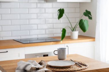 Kahvaltı için tabak ve fincanla ahşap masa üstü bulanık beyaz mutfağa karşı kesme tahtası ve sabah ışığında İskandinav tarzında bitki yetiştirme.