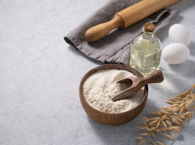 Tahta bir kasede yulaf ezmesi, kepçe, yumurta ve mavi arka planda merdane. Ev yapımı için doğal organik un. Metin için boş alan.