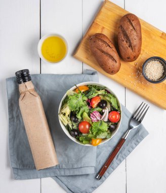 Ahşap arka planda, ekmek ve zeytinyağlı bir tabakta nefis sebze salatası. Sağlıklı beslenme konsepti. Üst görünüm.