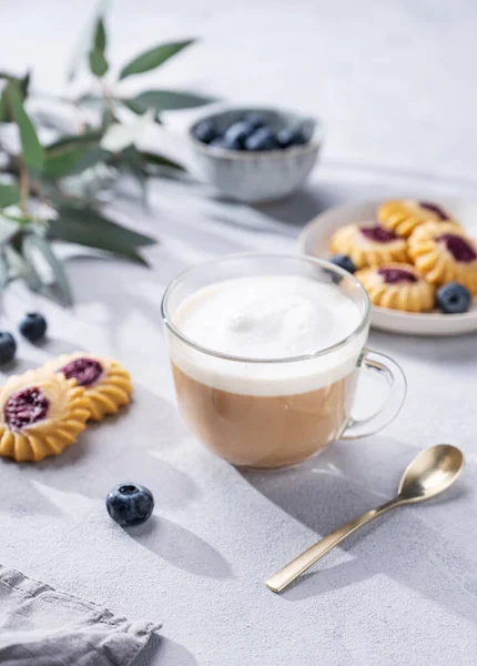 Kapuçino ya da sütlü sütlü latte kahve ev yapımı çilekli kurabiye ve okaliptüs dallı hafif bir arka planda yabanmersini. Bahar sabahı kahvaltısı hariç.. 