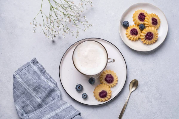 stock image Cappuccino or latte with milk foam in a cup with homemade  berry cookies and blueberries on a light background with gypsophila branches. Concept spring morning breakfast. Top view and copy space.