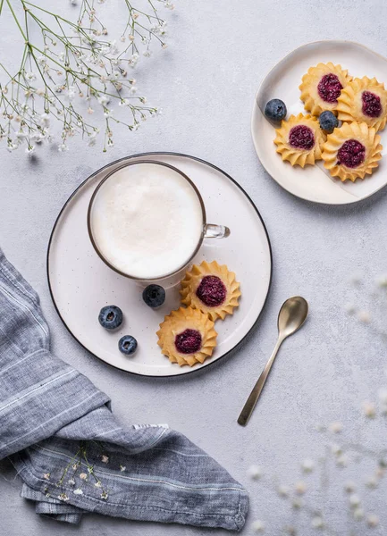 Kapuçino ya da sütlü sütlü latte kahve. El yapımı çilekli kurabiye ve yaban mersinli ve çigila dallı. Bahar sabahı kahvaltısı kavramı. Üst görünüm.