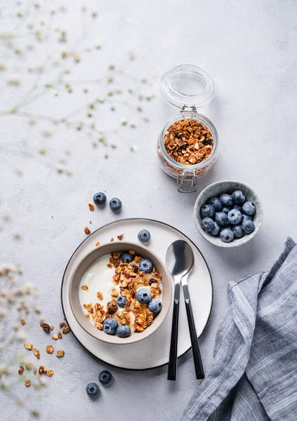 stock image The concept of a healthy breakfast of yogurt, granola and fresh blueberry on a blue background with flowers. Homemade diet and protein food. Top view and copy space.