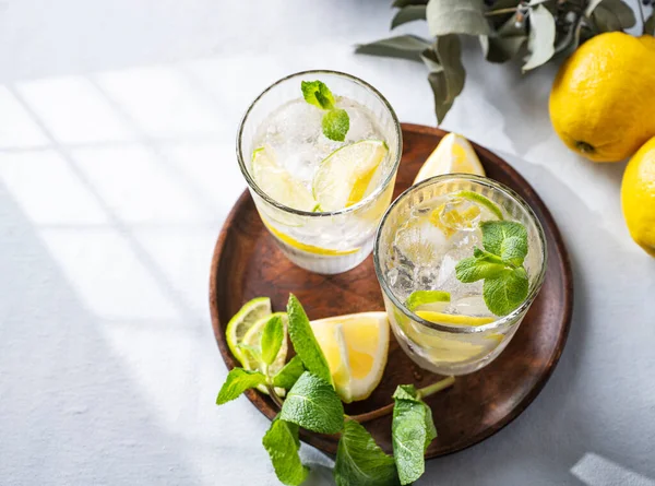 stock image Lemonade drink with fresh lemon, lime, mint and ice. Refreshing citrus mojito cocktail on a light background with shadow. Summer cold drinks concept. Top view and copy space.