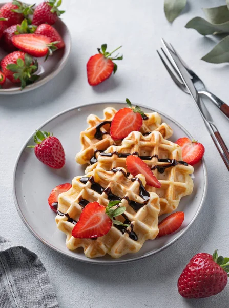 stock image Homemade soft waffles with fresh strawberries and chocolate topping in a plate on a light background close up. Traditional Belgian waffles. Healthy  breakfast. 