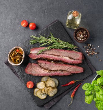 Izgara bbq göğüs eti dilimleri, jalapenolarla, otlarla ve salatalık turşusuyla birlikte koyu bir arka planda. Sigara tiryakisinde nefis bir lezzet. Üst görünüm.