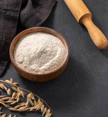 Yulaf unu, merdane iğnesi ve kuru dalla koyu bir arka planda peçeteyle. Organik pişirme malzemeleri. Ev yapımı ve sağlıklı yemek kavramı. Üst görünüm ve kopyalama alanı.